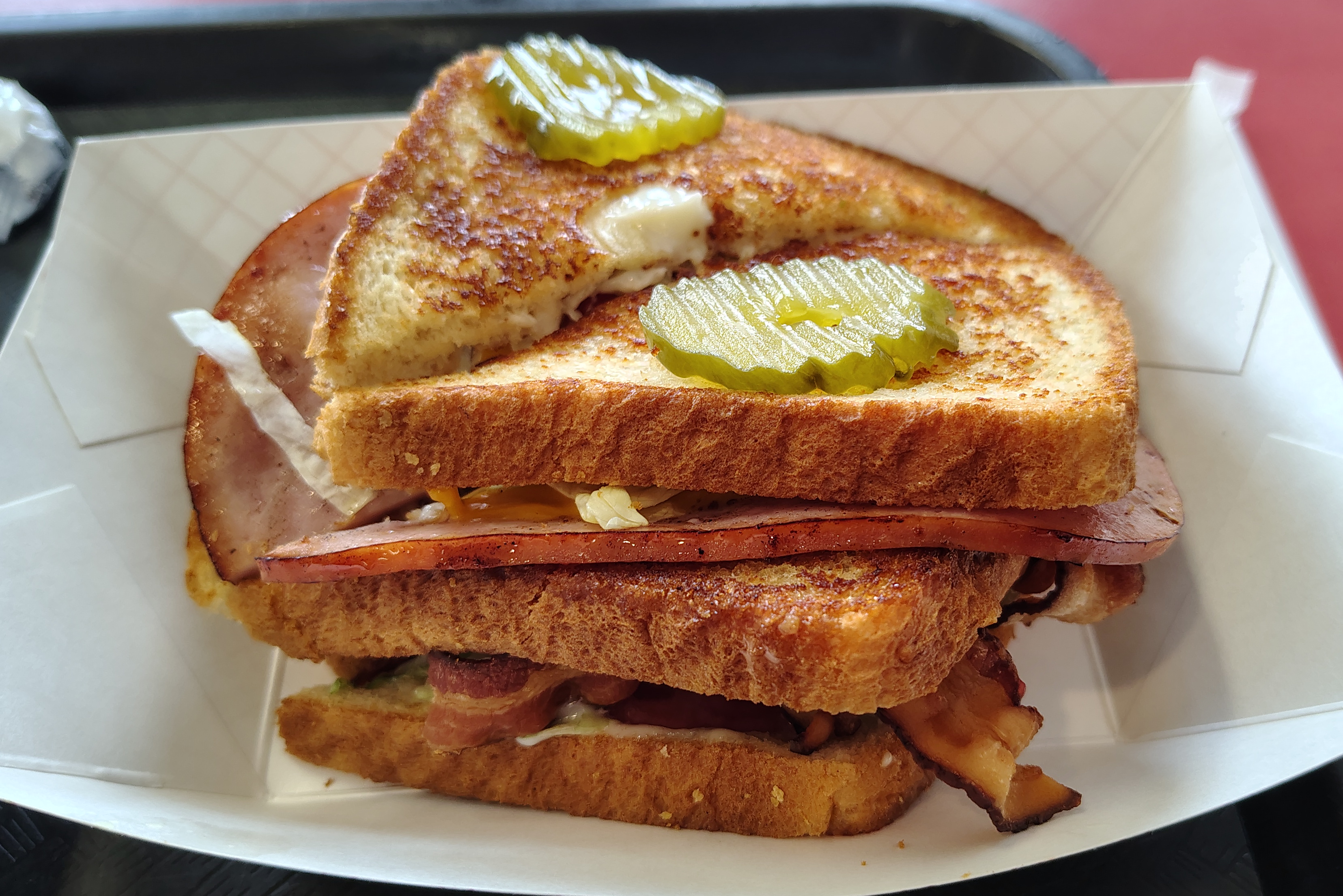 A delicious club sandwich with ham, bacon, american cheese, lettuce, and tomato between three pieces of toast